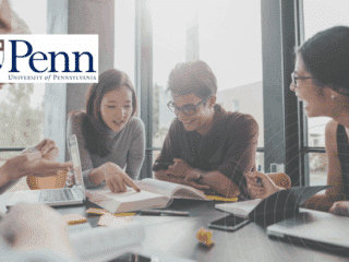 Groupe d’étudiants en pleine séance de travail collaboratif autour d’une table, avec ordinateurs portables et livres, dans une salle lumineuse de l’Université de Pennsylvanie (Penn), logo visible à l’arrière-plan.