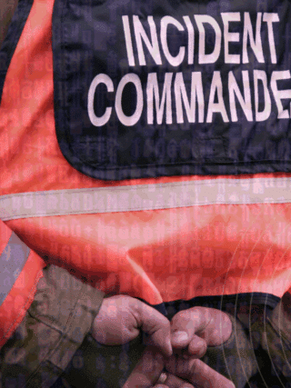 Vue rapprochée d’un commandant d’incident en tenue de gestion de crise, les mains croisées dans le dos, avec un gilet haute visibilité marqué « Incident Commander », sur fond de code informatique symbolisant la cybersécurité.