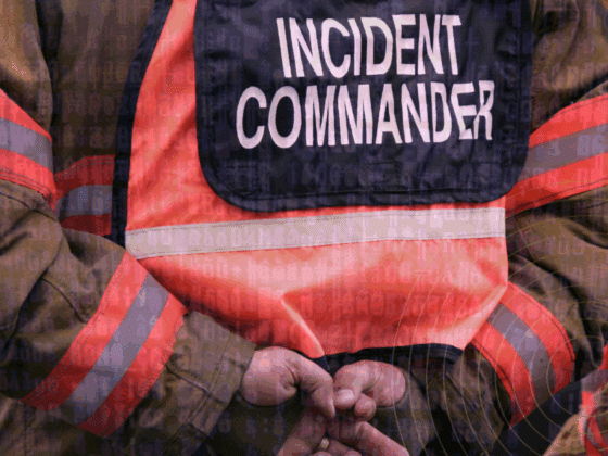 Vue rapprochée d’un commandant d’incident en tenue de gestion de crise, les mains croisées dans le dos, avec un gilet haute visibilité marqué « Incident Commander », sur fond de code informatique symbolisant la cybersécurité.