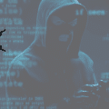 Un individu en cagoule et gants noirs se tient dans l’ombre, entouré de lignes de code bleu, évoquant une activité cybercriminelle.