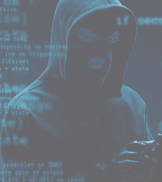 Un individu en cagoule et gants noirs se tient dans l’ombre, entouré de lignes de code bleu, évoquant une activité cybercriminelle.