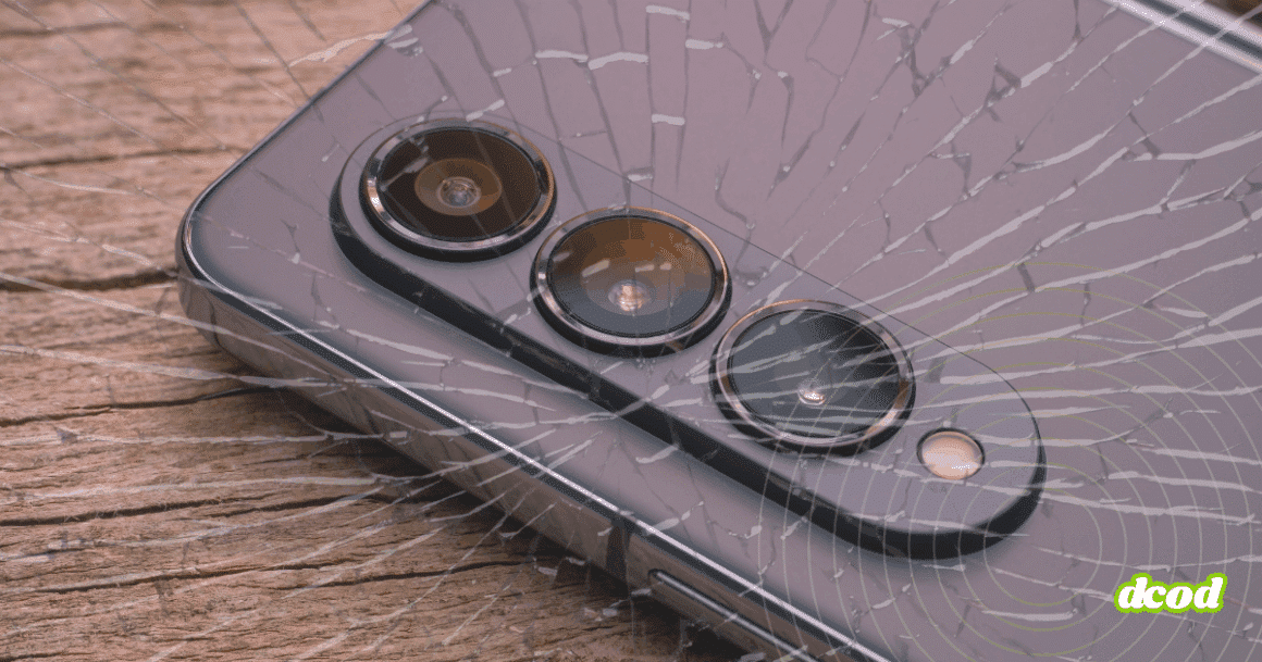 Gros plan sur un smartphone moderne avec triple capteur photo, posé sur du bois, recouvert d’un effet de verre fissuré symbolisant une faille ou une vulnérabilité. Logo "dcod" en bas à droite.