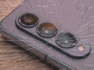 Gros plan sur un smartphone moderne avec triple capteur photo, posé sur du bois, recouvert d’un effet de verre fissuré symbolisant une faille ou une vulnérabilité. Logo "dcod" en bas à droite.