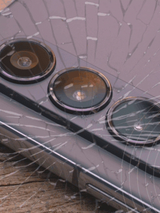 Gros plan sur un smartphone moderne avec triple capteur photo, posé sur du bois, recouvert d’un effet de verre fissuré symbolisant une faille ou une vulnérabilité. Logo "dcod" en bas à droite.