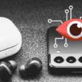 Un smartphone Samsung posé à côté d’écouteurs sans fil, avec une icône d’œil stylisé symbolisant la surveillance numérique.