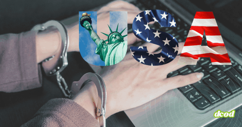 Mains menottées d'un cybercriminel posées sur un clavier d’ordinateur, avec le mot « USA » en surimpression illustré par la statue de la Liberté, le drapeau américain et des étoiles,