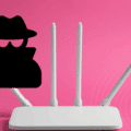 Un routeur blanc à antennes sur fond rose avec une silhouette noire de hacker symbolisant un détournement potentiel du réseau.