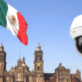 Grand drapeau mexicain flottant devant la cathédrale métropolitaine de Mexico, avec en premier plan une caméra de vidéosurveillance moderne illustrant l’essor des technologies de sécurité dans l’espace public.