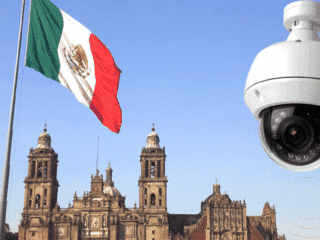 Grand drapeau mexicain flottant devant la cathédrale métropolitaine de Mexico, avec en premier plan une caméra de vidéosurveillance moderne illustrant l’essor des technologies de sécurité dans l’espace public.