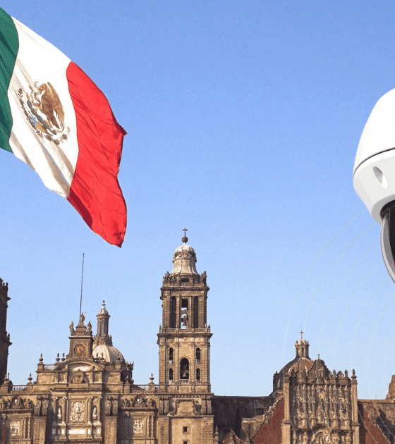 Grand drapeau mexicain flottant devant la cathédrale métropolitaine de Mexico, avec en premier plan une caméra de vidéosurveillance moderne illustrant l’essor des technologies de sécurité dans l’espace public.