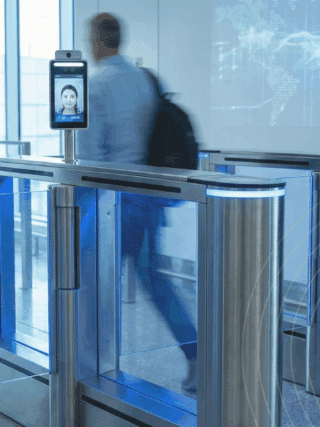 Des passagers flous franchissent des portiques de sécurité automatisés équipés d'écrans de reconnaissance faciale dans un aéroport.