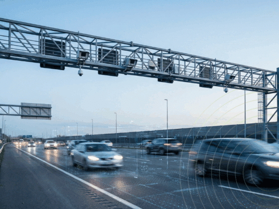 Un portique métallique équipé de caméras et de capteurs surplombe une autoroute à plusieurs voies avec des voitures en mouvement.
