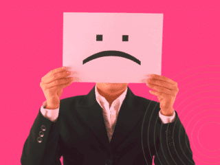 Une personne en costume tenant devant son visage une feuille avec un visage triste, symbolisant une potentielle menace interne en entreprise.