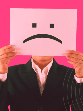 Une personne en costume tenant devant son visage une feuille avec un visage triste, symbolisant une potentielle menace interne en entreprise.