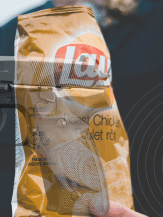 Un système AI confond un paquet de chips avec une arme dans un lycée 25 Montage photographique représentant un paquet de chips Lay’s saveur poulet rôti tenu par une personne en costume, avec une superposition d’image d’un pistolet semi-automatique, créant un contraste visuel fort entre aliment et arme à feu.