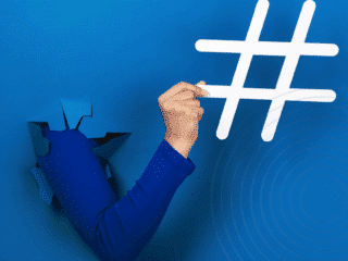 Bras sortant d’une déchirure dans un mur bleu vif, tenant un grand symbole de hashtag blanc, illustrant le pouvoir des réseaux sociaux et des tendances numériques.