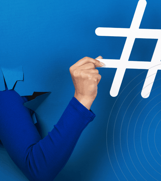 Bras sortant d’une déchirure dans un mur bleu vif, tenant un grand symbole de hashtag blanc, illustrant le pouvoir des réseaux sociaux et des tendances numériques.