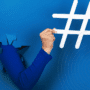 Bras sortant d’une déchirure dans un mur bleu vif, tenant un grand symbole de hashtag blanc, illustrant le pouvoir des réseaux sociaux et des tendances numériques.