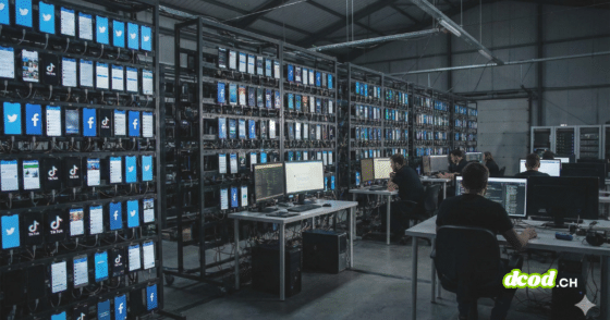 Photographie d'illustration au format paysage 16/9 montrant l'intérieur d'un vaste entrepôt sombre. Des centaines de smartphones sont alignés sur des racks métalliques, leurs écrans allumés affichant des applications de réseaux sociaux comme Facebook, TikTok et Twitter. Au premier plan et en arrière-plan, des personnes sont assises devant des postes de travail équipés d'ordinateurs, surveillant et contrôlant l'activité des téléphones. L'ambiance est industrielle et technologique, illustrant une opération d'influence numérique à grande échelle.