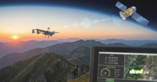 Photographie d'illustration au format paysage 16/9 montrant un drone volant au-dessus de montagnes au coucher du soleil. Un signal graphique relie le drone à un satellite en orbite terrestre, illustrant le pilotage via GPS. Un écran de contrôle affichant des données GPS et une carte est visible au premier plan.