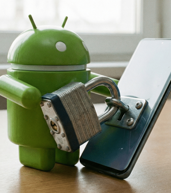 Une figurine de la mascotte Android verte en plastique est représentée, "verrouillant" un smartphone moderne éteint avec un gros cadenas métallique. L'image symbolise la sécurité et la protection des données sur les appareils mobiles.