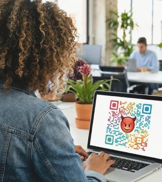 Une femme de dos à un bureau tape sur un ordinateur portable. L'écran affiche un grand QR code multicolore avec un emoji diable rouge au centre, illustrant un lien malveillant.