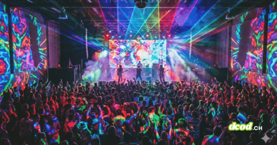 Foule dansant lors d'un concert animé, la scène et les murs étant éclairés par des projections lumineuses psychédéliques et des faisceaux laser de toutes les couleurs.