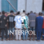 Groupe de personnes vues de dos devant un bâtiment, avec le logo d’Interpol au premier plan, illustrant une action policière internationale.