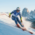 Photographie d'une skieuse alpine italienne en pleine action lors d'une descente de slalom géant, portant le dossard de Milan Cortina 2026, avec les montagnes des Dolomites en arrière-plan.
