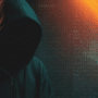 Illustration pour la veille sur les fuites de données : une silhouette de hacker encapuchonné dans l'ombre, sur fond de code informatique bleu, est traversée par des faisceaux lumineux diagonaux orange intenses évoquant une alerte de sécurité ou une brèche active.