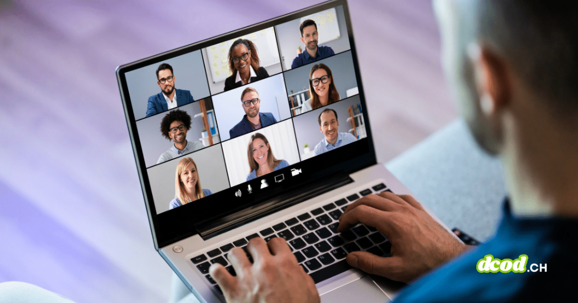 Vue en plongée par-dessus l'épaule d'une personne travaillant sur un ordinateur portable. L'écran affiche une galerie de visioconférence avec neuf participants souriants dans un cadre professionnel. Un filigrane 'dcod.ch' est visible en bas à droite.