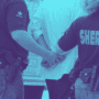Photographie teintée en bleu montrant deux agents du bureau du shérif, de dos, en train de menotter une personne. On aperçoit leurs uniformes marqués "SHERIFF" et leurs ceinturons d'équipement.