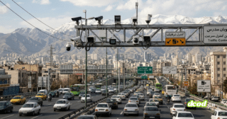 Une vue panoramique en hauteur de l'autoroute Modares à Téhéran, bondée de voitures. Un grand portique métallique traverse la route, supportant de nombreuses caméras de surveillance et radars de vitesse, avec la ville dense et des montagnes enneigées en arrière-plan.