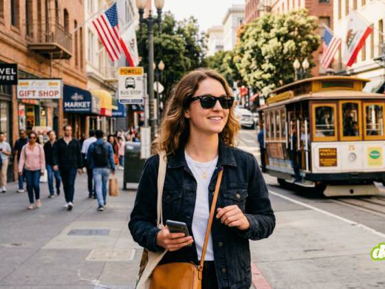 Plan moyen d'une jeune femme marchant dans une rue animée de San Francisco, portant des lunettes de soleil noires de style Ray-Ban et tenant son smartphone. Derrière elle, on aperçoit un cable car et une foule de piétons. Cette image illustre la scène de l'article sur l'application Nearby Glasses, qui alerte sur la présence de lunettes intelligentes Meta Ray-Ban.