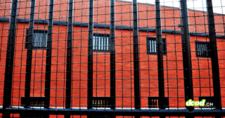 Illustration de l'incarcération injuste : vue de barreaux de prison sur fond de mur en briques rouges, évoquant les conséquences d'une erreur de reconnaissance faciale.