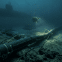 Photographie sous-marine au format paysage montrant un épais câble de fibre optique noir reposant sur le fond marin accidenté. En arrière-plan, un sous-marin militaire sombre est en maraude, tandis qu'un drone sous-marin (ROV) explore la zone avec des projecteurs allumés. L'ambiance est sombre et froide, illustrant les infrastructures critiques en zone de conflit.