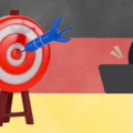 Illustration symbolique représentant un pirate informatique masqué derrière un ordinateur ciblant le drapeau allemand avec une fléchette. L'Allemagne devient la cible numéro 1 de la cyber-extorsion en Europe.