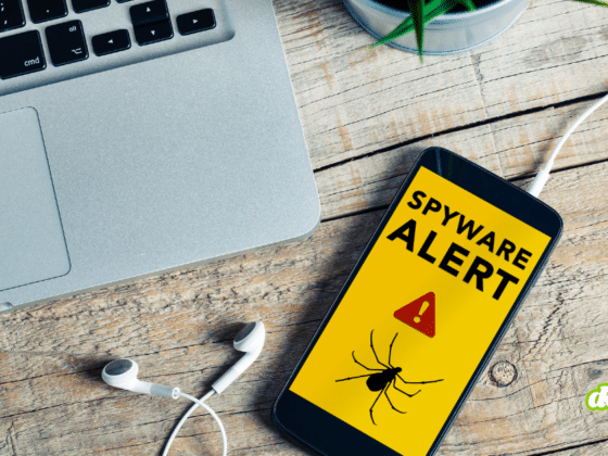 Illustration d'un smartphone iOS affichant un message de sécurité "Spyware Alert" avec une icône d'araignée sur un bureau en bois, symbolisant l'alerte de WhatsApp concernant les 200 victimes d'un spyware italien infiltré via une fausse application.