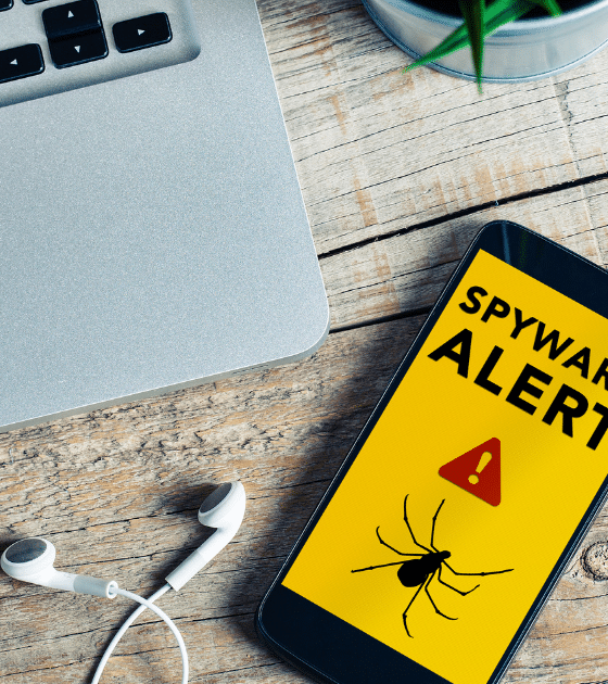Illustration d'un smartphone iOS affichant un message de sécurité "Spyware Alert" avec une icône d'araignée sur un bureau en bois, symbolisant l'alerte de WhatsApp concernant les 200 victimes d'un spyware italien infiltré via une fausse application.