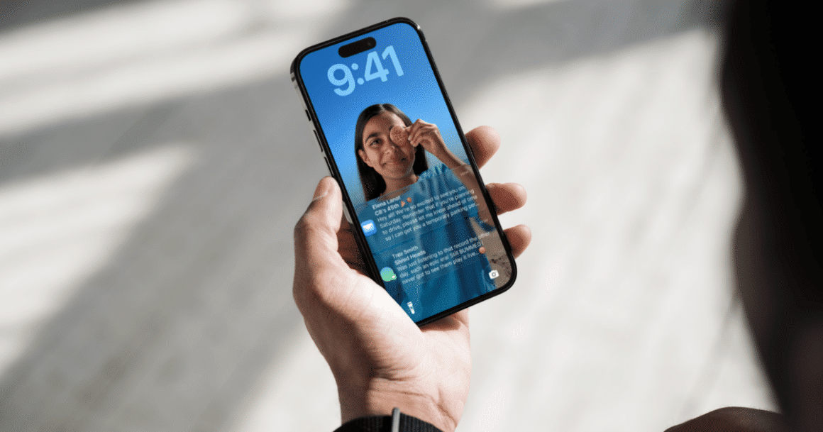Photographie d'une main tenant un iPhone dont l'écran de verrouillage iOS affiche plusieurs notifications, illustrant le nouveau système d'alerte urgente de sécurité déployé par Apple.
