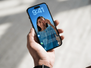 Photographie d'une main tenant un iPhone dont l'écran de verrouillage iOS affiche plusieurs notifications, illustrant le nouveau système d'alerte urgente de sécurité déployé par Apple.