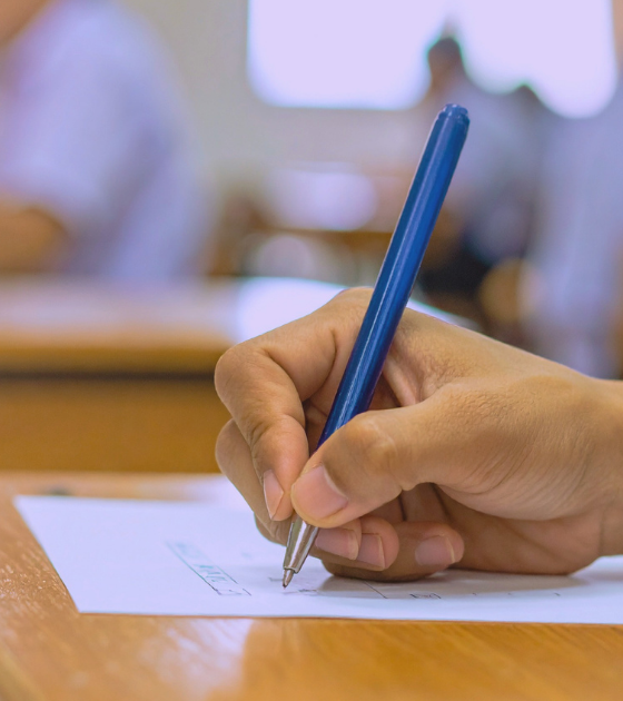 Main d'un étudiant rédigeant sa copie pour illustrer comment le piratage du portail scolaire Canvas paralyse les examens.