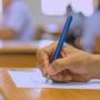 Main d'un étudiant rédigeant sa copie pour illustrer comment le piratage du portail scolaire Canvas paralyse les examens.
