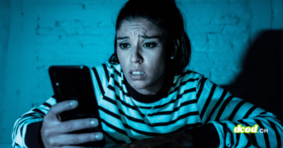 Une femme exprime de l'inquiétude en consultant son smartphone dans l'obscurité, illustrant le cyberharcèlement que les agents IA automatisent désormais lors d'une attaque numérique ciblée.