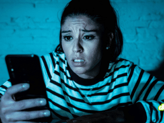 Une femme exprime de l'inquiétude en consultant son smartphone dans l'obscurité, illustrant le cyberharcèlement que les agents IA automatisent désormais lors d'une attaque numérique ciblée.