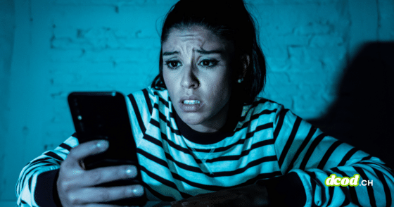 Une femme exprime de l'inquiétude en consultant son smartphone dans l'obscurité, illustrant le cyberharcèlement que les agents IA automatisent désormais lors d'une attaque numérique ciblée.