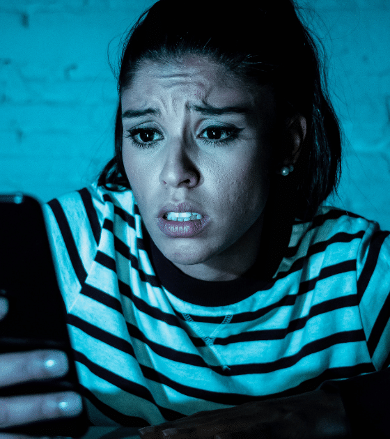 Une femme exprime de l'inquiétude en consultant son smartphone dans l'obscurité, illustrant le cyberharcèlement que les agents IA automatisent désormais lors d'une attaque numérique ciblée.