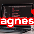 Un ordinateur portable ouvert affiche des lignes de code informatique sur fond noir. À gauche de l'écran se trouve le manchot mascotte de Linux, et à droite, un chapeau rouge de type fedora. Le mot "Fragnesia" est inscrit en grandes lettres blanches entourées de rouge au premier plan. Dans le coin inférieur droit, le logo d'un média d'information est visible.