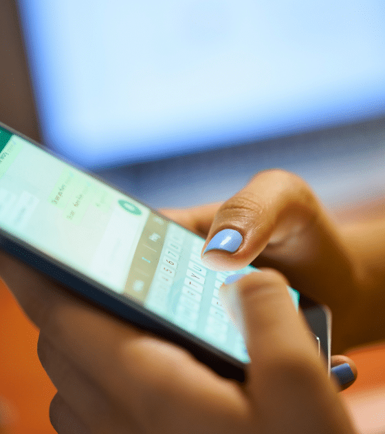 Une utilisatrice (ongles bleus) tient un smartphone affichant l'interface de Meta AI Incognito chat avec le clavier ouvert, illustrant l'utilisation du nouveau mode incognito de Meta. En arrière-plan flou, un ordinateur portable montre du code informatique, évoquant le contexte technique des experts DCOD analysant les paramètres de confidentialité et de chiffrement. Le logo dcod.ch est présent dans le