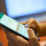 Une utilisatrice (ongles bleus) tient un smartphone affichant l'interface de Meta AI Incognito chat avec le clavier ouvert, illustrant l'utilisation du nouveau mode incognito de Meta. En arrière-plan flou, un ordinateur portable montre du code informatique, évoquant le contexte technique des experts DCOD analysant les paramètres de confidentialité et de chiffrement. Le logo dcod.ch est présent dans le